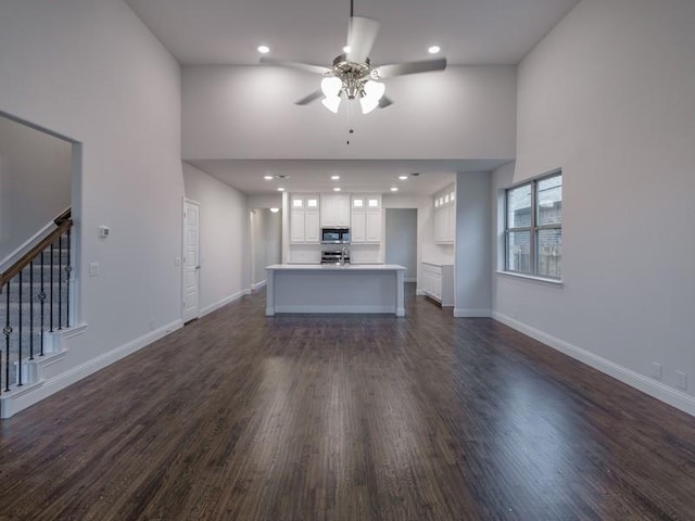 unfurnished living room with ceiling fan, a towering ceiling, and dark hardwood / wood-style flooring