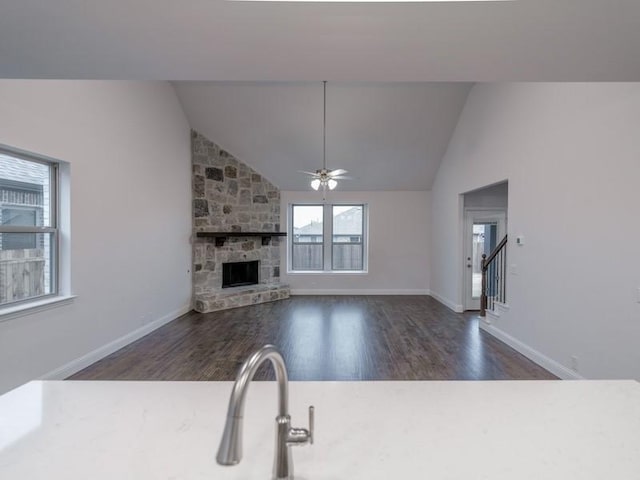 unfurnished living room with dark hardwood / wood-style floors, ceiling fan, a stone fireplace, and vaulted ceiling