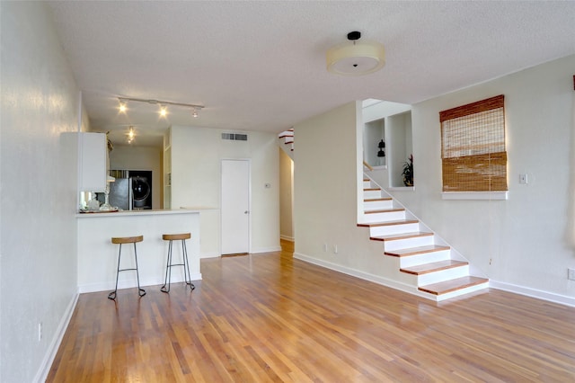 kitchen with a breakfast bar area, a textured ceiling, light wood-type flooring, fridge, and white cabinets