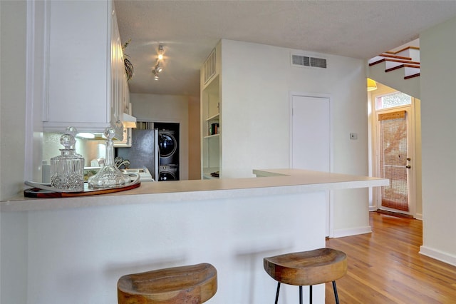 kitchen featuring a kitchen bar, stacked washer / drying machine, kitchen peninsula, a textured ceiling, and light hardwood / wood-style flooring