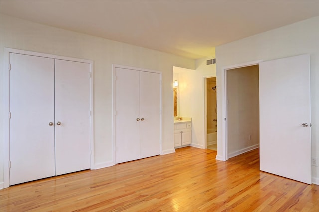 unfurnished bedroom featuring ensuite bath, light hardwood / wood-style flooring, and multiple closets