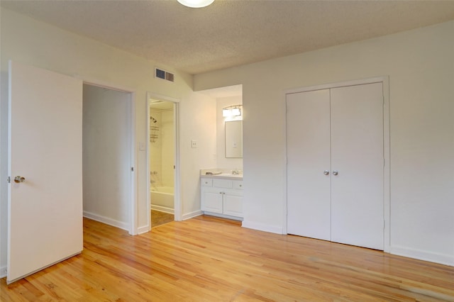 unfurnished bedroom featuring ensuite bathroom, sink, a textured ceiling, a closet, and light hardwood / wood-style floors