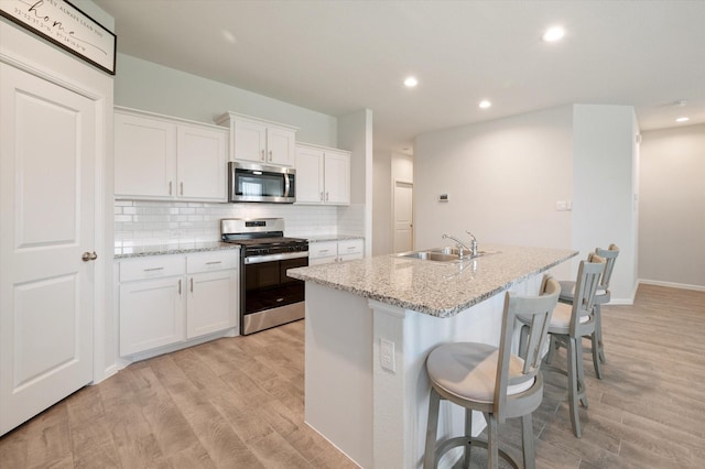 kitchen featuring white cabinetry, light stone counters, an island with sink, and appliances with stainless steel finishes