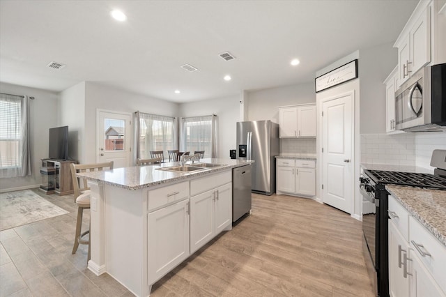 kitchen featuring sink, stainless steel appliances, a kitchen island with sink, decorative backsplash, and white cabinets