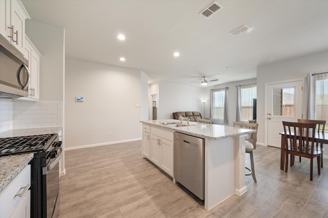 kitchen with appliances with stainless steel finishes, a breakfast bar, white cabinetry, an island with sink, and light stone counters