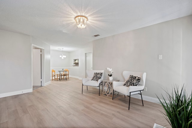 living area featuring a textured ceiling, a notable chandelier, and light hardwood / wood-style floors