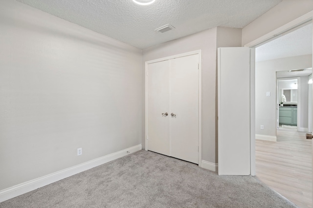 unfurnished bedroom featuring light colored carpet, a textured ceiling, and a closet