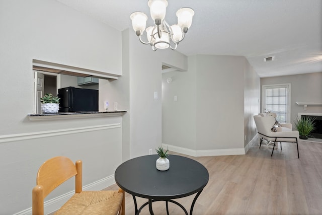 dining space with an inviting chandelier, a textured ceiling, and light wood-type flooring