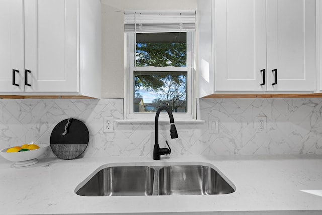 room details with white cabinetry, sink, light stone counters, and backsplash