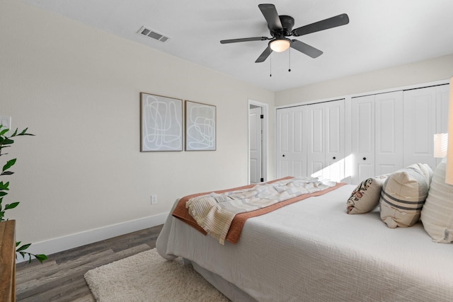 bedroom featuring dark wood-type flooring, ceiling fan, and two closets