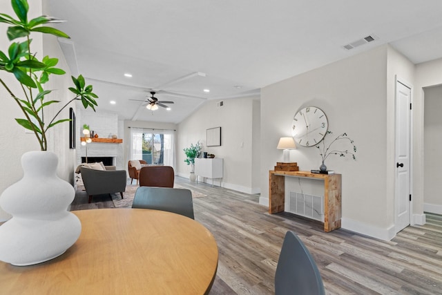 dining space with ceiling fan, light hardwood / wood-style floors, vaulted ceiling, and a brick fireplace