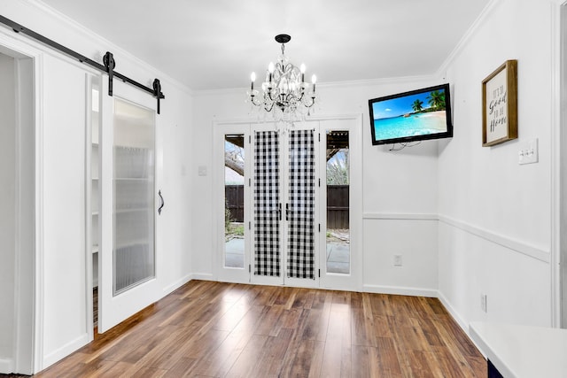 unfurnished dining area featuring hardwood / wood-style flooring, ornamental molding, a barn door, french doors, and a chandelier