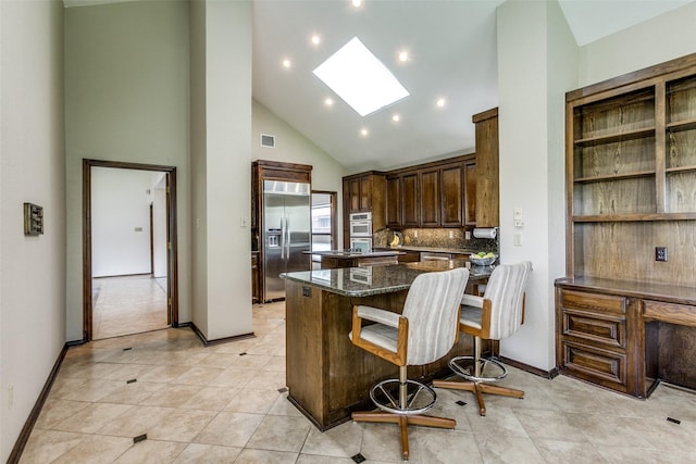 kitchen with built in refrigerator, a skylight, high vaulted ceiling, decorative backsplash, and dark stone counters