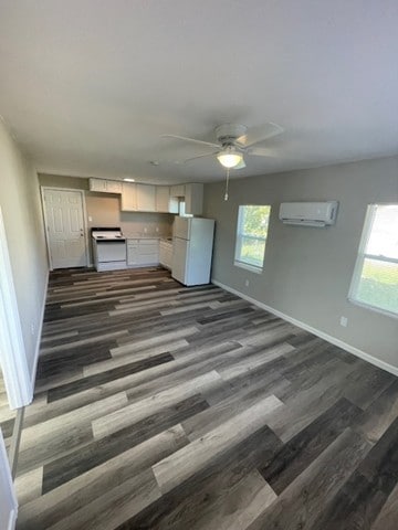 unfurnished living room with dark hardwood / wood-style flooring, a wealth of natural light, ceiling fan, and a wall unit AC