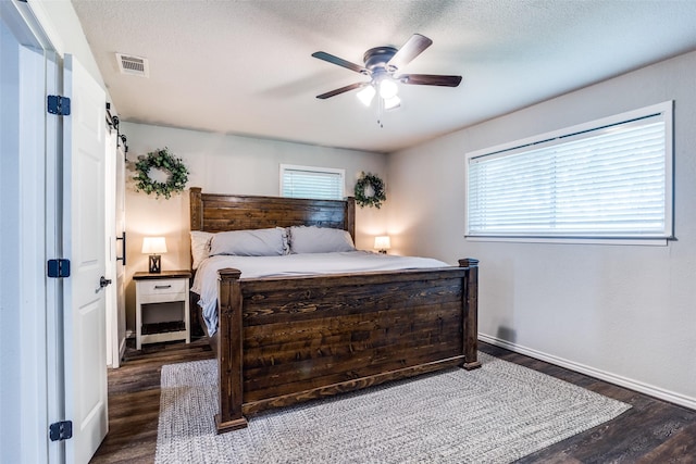 bedroom with dark hardwood / wood-style floors, a textured ceiling, a barn door, and ceiling fan