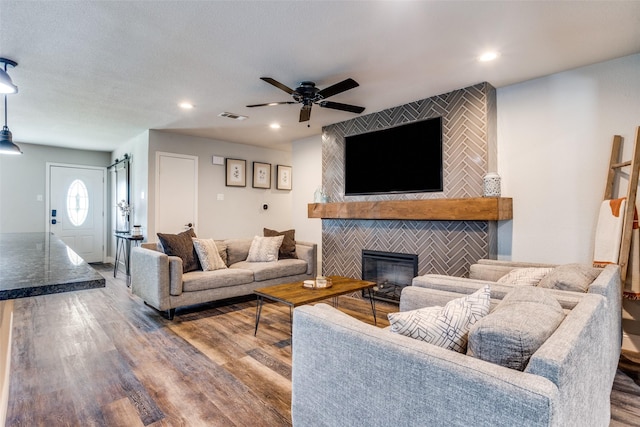 living room with hardwood / wood-style flooring, ceiling fan, and a tiled fireplace