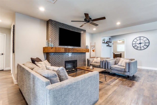 living room with a tiled fireplace, light hardwood / wood-style floors, and ceiling fan