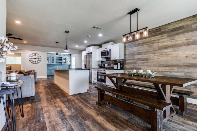 kitchen with white cabinetry, appliances with stainless steel finishes, wooden walls, and pendant lighting