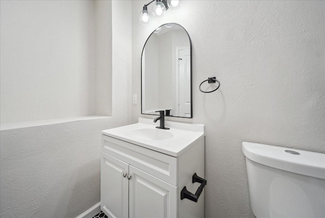 half bath with toilet, a textured wall, and vanity