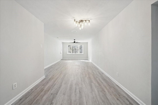 unfurnished living room with ceiling fan, a textured ceiling, wood finished floors, visible vents, and baseboards