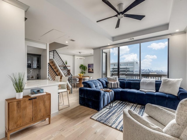 living room featuring light hardwood / wood-style flooring, a raised ceiling, and ceiling fan