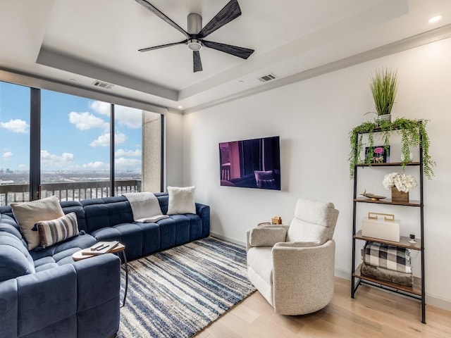 living room with a raised ceiling, crown molding, hardwood / wood-style flooring, and ceiling fan