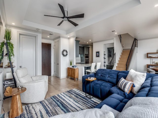 living room with ceiling fan, a tray ceiling, and light wood-type flooring