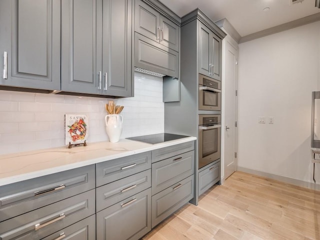 kitchen featuring gray cabinets, black electric stovetop, light stone countertops, stainless steel double oven, and light wood-type flooring