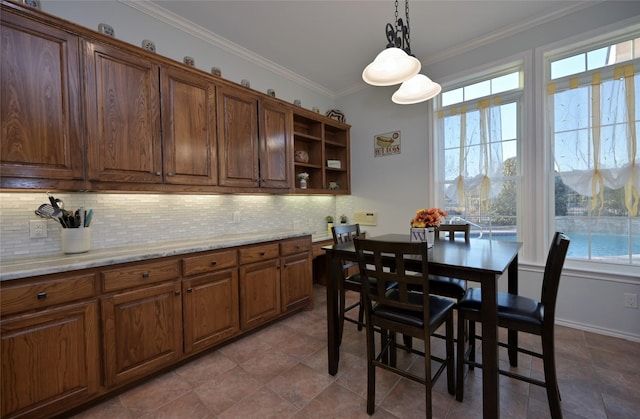 kitchen featuring light stone counters, backsplash, decorative light fixtures, and ornamental molding