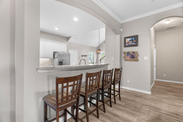 bar with backsplash, stainless steel refrigerator with ice dispenser, light stone counters, white cabinets, and light wood-type flooring