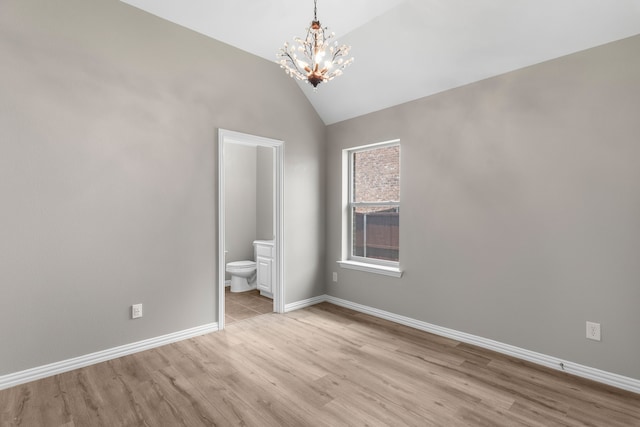 unfurnished bedroom featuring a notable chandelier, vaulted ceiling, ensuite bath, and light wood-type flooring