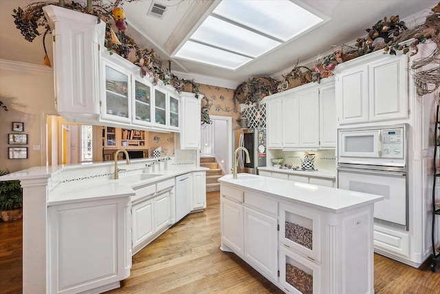 kitchen featuring a kitchen island, white cabinets, white appliances, and kitchen peninsula