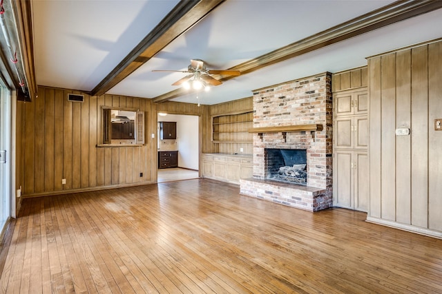 unfurnished living room with built in features, beamed ceiling, ceiling fan, a fireplace, and light hardwood / wood-style floors