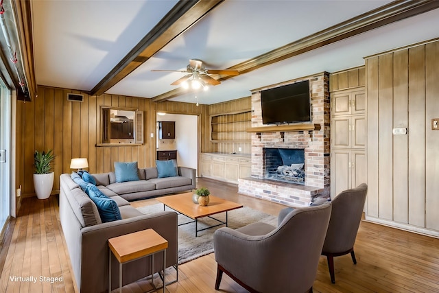 living room with beamed ceiling, ceiling fan, a brick fireplace, and light wood-type flooring