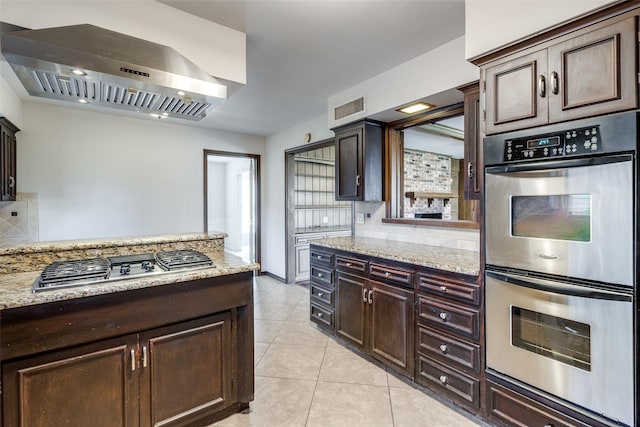 kitchen with appliances with stainless steel finishes, backsplash, light tile patterned floors, light stone countertops, and wall chimney exhaust hood