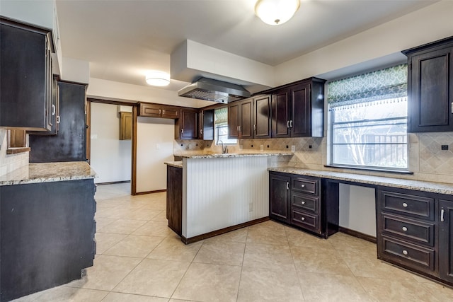 kitchen with light stone countertops, dark brown cabinets, sink, and decorative backsplash