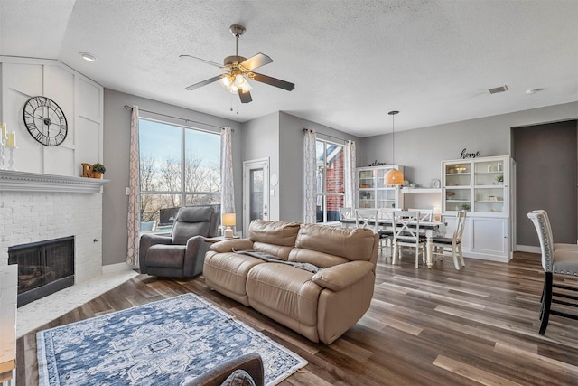 living room with plenty of natural light, a brick fireplace, vaulted ceiling, and a textured ceiling