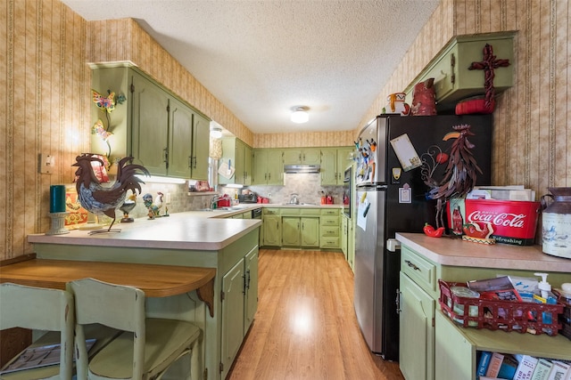 kitchen featuring stainless steel refrigerator, sink, green cabinetry, a textured ceiling, and light wood-type flooring