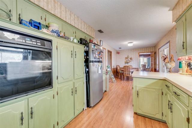 kitchen featuring stainless steel refrigerator, light hardwood / wood-style floors, kitchen peninsula, a textured ceiling, and oven