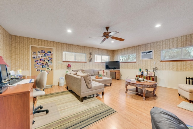 living room featuring radiator, light hardwood / wood-style flooring, ceiling fan, a wall mounted air conditioner, and a textured ceiling