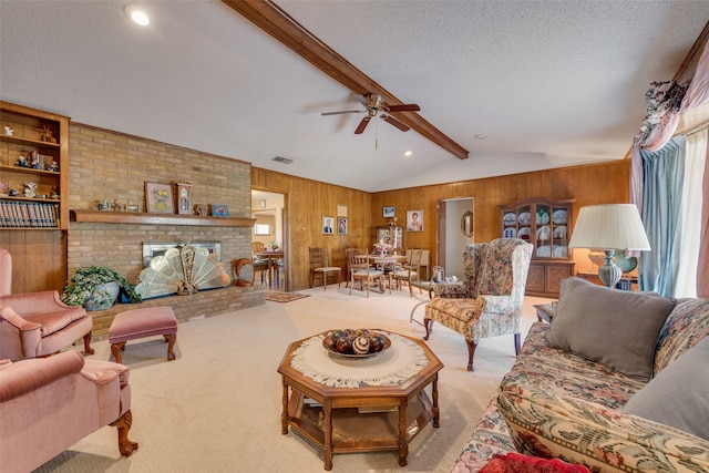 carpeted living room with vaulted ceiling with beams, wood walls, a brick fireplace, a textured ceiling, and ceiling fan