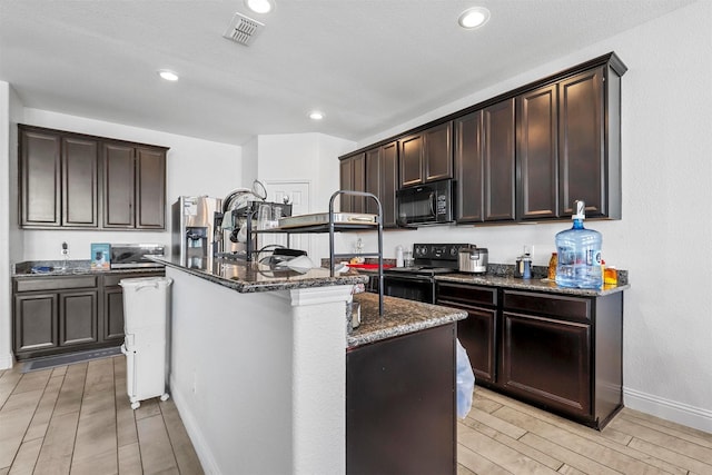 kitchen with dark brown cabinetry, black appliances, dark stone counters, and a center island with sink