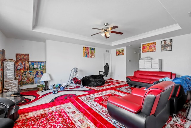 living room with a raised ceiling, crown molding, and ceiling fan