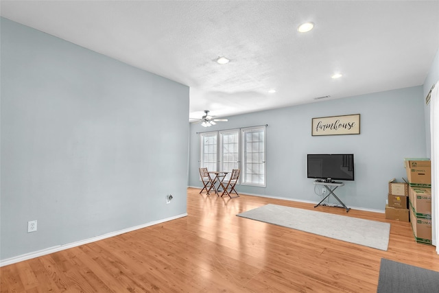 living room with a textured ceiling, ceiling fan, and light hardwood / wood-style flooring