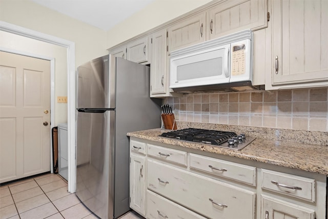 kitchen with light tile patterned floors, appliances with stainless steel finishes, backsplash, light stone countertops, and washer / clothes dryer