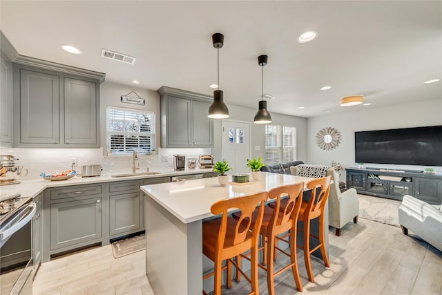 kitchen featuring a kitchen bar, sink, a center island, gray cabinets, and stainless steel stove