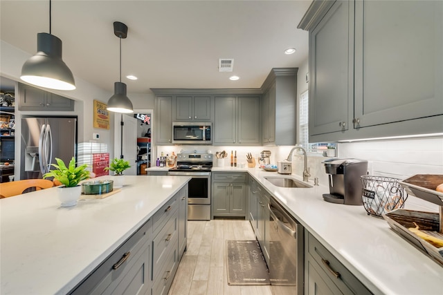 kitchen featuring stainless steel appliances, decorative light fixtures, sink, and gray cabinetry