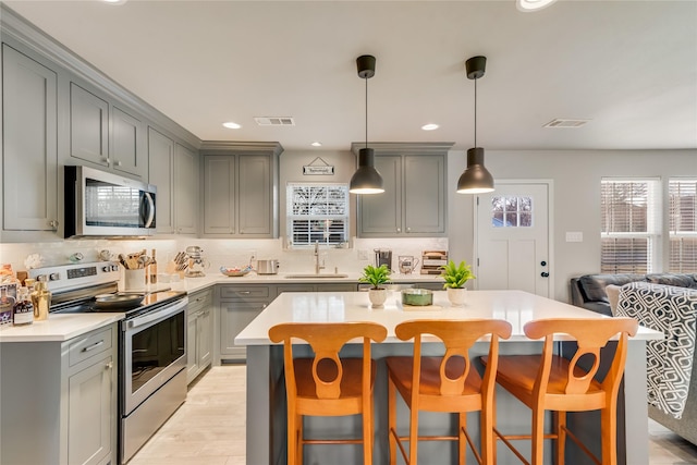 kitchen with sink, gray cabinetry, hanging light fixtures, stainless steel appliances, and a kitchen bar