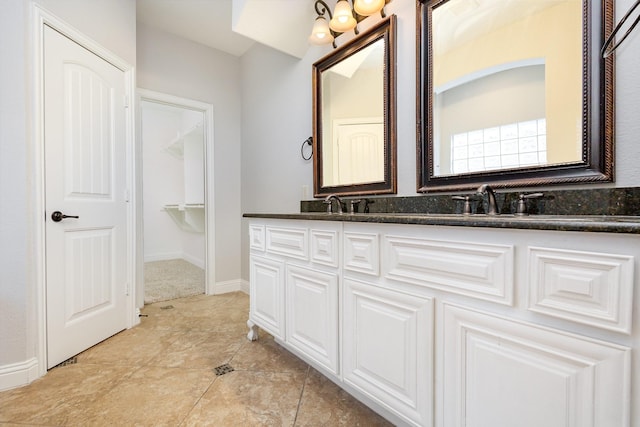 bathroom with double vanity, a walk in closet, and baseboards