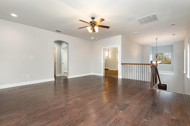 empty room with baseboards, visible vents, arched walkways, and dark wood-style flooring